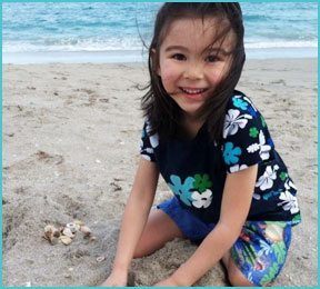 girl in flower patterned shirt outside at the beach smiling