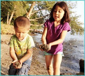 boy and girl playing on a beach with sand, water and trees