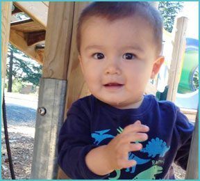 baby boy outdoors at a playground sitting by play equipment