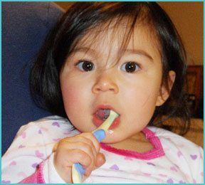 baby girl with toothbrush in mouth brushing teeth