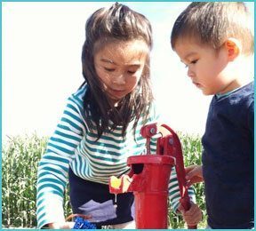 boy and girl playing outside with red water pump
