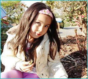 little girl outside in white goat and with plant in hand