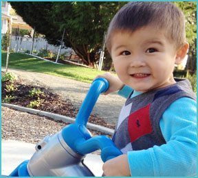 little boy with tricycle outside playing and smiling