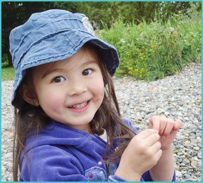 little girl with hat and purple sweatshirt outside smiling