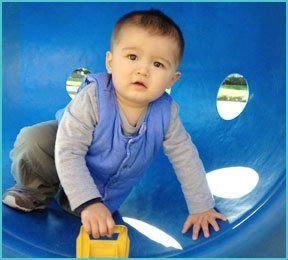 little boy with toy outdoors in blue plastic play equipment with holes